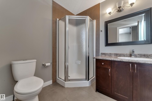 Corner shower with a glass enclosure, single vanity with a stone countertop, dark wood-finish cabinetry, and a framed mirror - 11421 82 Street Nw, Edmonton, AB 