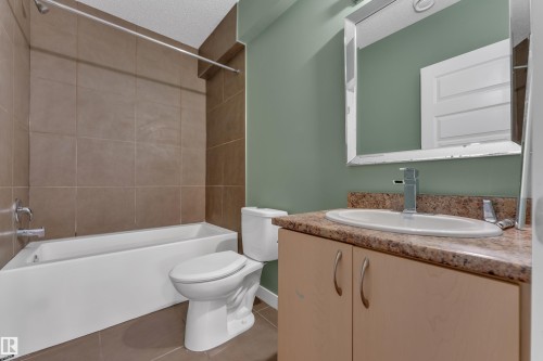 Bathroom featuring an integrated bathtub and shower with full-height tile surround, a vanity with a surface-mounted sink, and a framed mirror - 11421 82 Street Nw, Edmonton, AB 