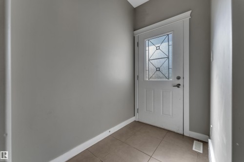 Welcoming entryway featuring a white six-panel door with geometric glass detailing, neutral gray walls, and tile flooring - 11421 82 Street Nw, Edmonton, AB 