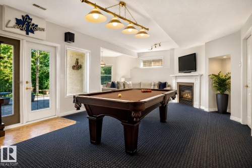 Lower level recreation area featuring a built-in fireplace with white mantel, wall-mounted television, and direct outdoor access through French doors - 941 Picard Drive Nw, Edmonton, AB 