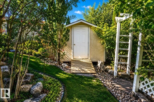 Landscaped exterior featuring a storage shed with a ramp, a manicured lawn, a rock border, and a white trellis - 941 Picard Drive Nw, Edmonton, AB 