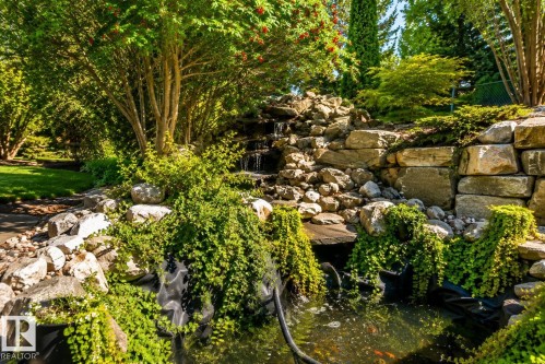 Water feature with cascading falls and a pond, surrounded by lush plantings and natural stone hardscaping - 941 Picard Drive Nw, Edmonton, AB 
