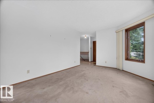 Wall-to-wall carpeting with solid baseboards, a wood-framed window, and a wooden banister - 2907 49 Street Nw, Edmonton, AB 