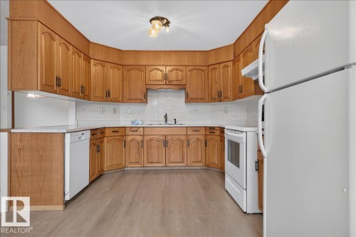 U-shaped kitchen with wood-finish cabinetry, light-toned countertops, tile backsplash, and light wood-finish flooring - 2907 49 Street Nw, Edmonton, AB 