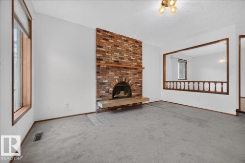 Brick fireplace with hearth, wood mantle, window with wood trim, wall-mounted light fixture, and carpet flooring - 2907 49 Street Nw, Edmonton, AB 