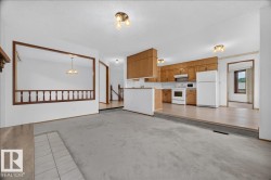 Carpeted living area with tile hearth, recessed kitchen with wood-finish cabinetry, and a wood-railed half-wall - 