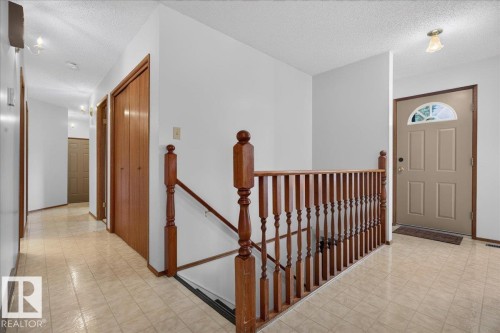 Tiled flooring throughout, wood-finish interior doors, wooden staircase railing, and a light-colored entry door with an arched transom window - 2907 49 Street Nw, Edmonton, AB 