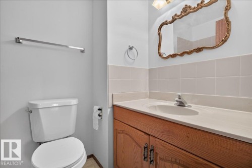 Bathroom featuring a wood-finish vanity with an undermount sink, ceramic tile backsplash, and chrome fixtures - 2907 49 Street Nw, Edmonton, AB 