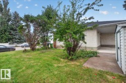 Stucco exterior with a covered carport, pitched shingle roof, and a detached storage shed - 