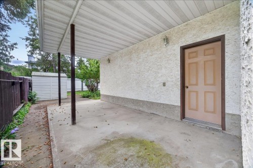 Covered concrete patio with stucco exterior, paneled door, exterior wall lighting, and a partial privacy fence - 2907 49 Street Nw, Edmonton, AB 
