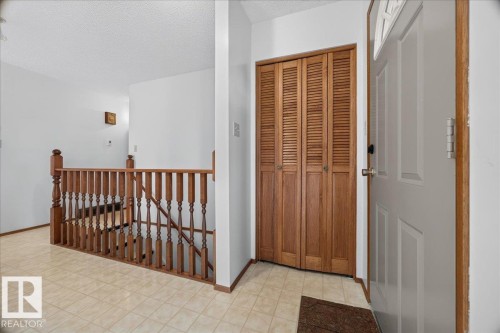 Entryway featuring tile flooring, wood louvered bi-fold closet doors, a white paneled entry door with decorative glass, and a wood staircase with turned balusters - 2907 49 Street Nw, Edmonton, AB 