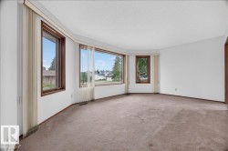 Bay window configuration with multiple windows, wood-finish window frames, and neutral carpeting - 