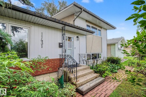 Front exterior featuring multi-level architecture, a brick accent wall, white siding, and an ornate wrought iron railing at the entrance - 11431 51 Avenue Nw, Edmonton, AB 