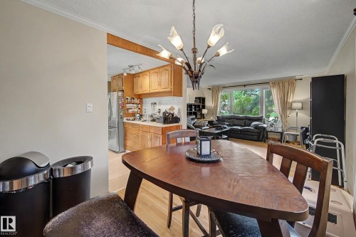 Open concept dining area with a multi-light chandelier, light wood-finish flooring, and crown molding - 11431 51 Avenue Nw, Edmonton, AB 