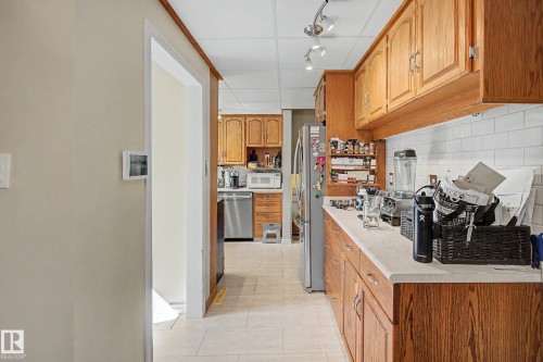 Galley kitchen with wood cabinetry, light countertops, white subway tile backsplash, and stainless steel appliances - 11431 51 Avenue Nw, Edmonton, AB 