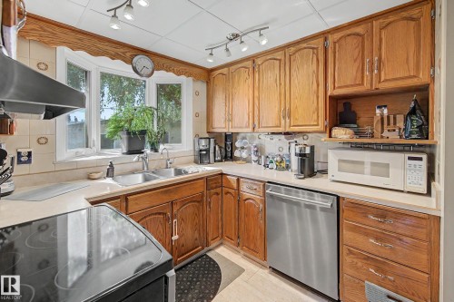 Wood cabinetry, light-toned countertops, stainless steel dishwasher, and track lighting - 11431 51 Avenue Nw, Edmonton, AB 