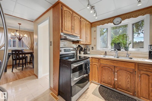 Kitchen featuring wood cabinetry, a bay window, and a stainless steel double basin sink - 11431 51 Avenue Nw, Edmonton, AB 