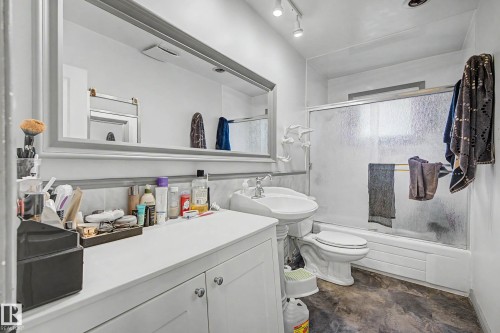 White vanity with undermount sink, built-in mirror with decorative frame, track lighting, and a shower-tub combination with sliding glass doors - 11431 51 Avenue Nw, Edmonton, AB 