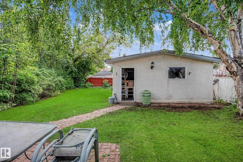 Expansive green space featuring a detached auxiliary building with an exterior light fixture, a paved pathway, and mature trees - 11431 51 Avenue Nw, Edmonton, AB 