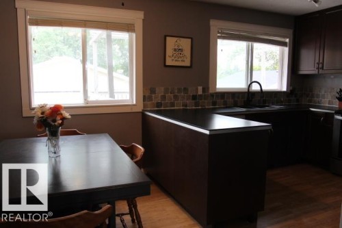 Kitchen featuring dark wood-finish cabinetry, black countertops, and a tiled backsplash - 64 Apache Crescent, Leduc, AB 