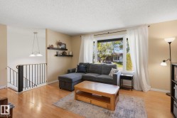 Hardwood-style flooring, large picture window, suspended ceiling light fixture, black metal stair railing, and dual floating wall shelves - 