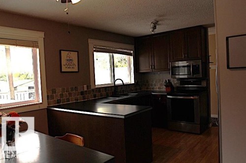 U-shaped kitchen counter with dark cabinetry, stainless steel appliances, and a tiled backsplash - 64 Apache Crescent, Leduc, AB 
