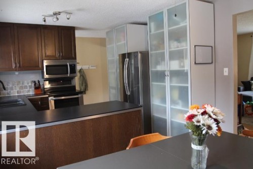 Kitchen featuring dark wood cabinetry, stainless steel appliances, and a tiled backsplash - 64 Apache Crescent, Leduc, AB 