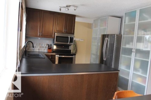 Kitchen featuring rich wood-finish cabinetry, a black counter surface, and a mosaic tile backsplash - 64 Apache Crescent, Leduc, AB 