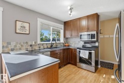Kitchen featuring wood-finish flooring, dark cabinetry, stainless steel appliances, and a tiled backsplash - 