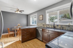Kitchen featuring wood-finish flooring, dark wood cabinetry, dark countertops, a stone tile backsplash, and a double basin sink with a black faucet - 
