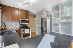 Kitchen featuring wood-finish cabinetry, stainless steel appliances, dark countertops, and a tiled backsplash - 