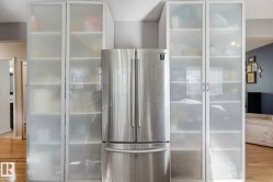 Stainless steel refrigerator with a bottom freezer, flanked by built-in storage units with frosted glass doors and multiple shelves - 