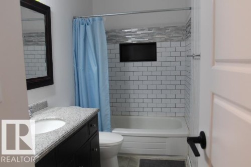 Bathroom featuring a white subway tile shower surround with an accent mosaic tile band, a recessed shower niche, and a vanity with a white oval sink and granite countertop - 64 Apache Crescent, Leduc, AB 