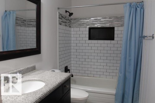 Granite-style countertop with undermount sink, dark wood vanity, subway tile shower surround with accent tile, and recessed shower niche - 64 Apache Crescent, Leduc, AB 