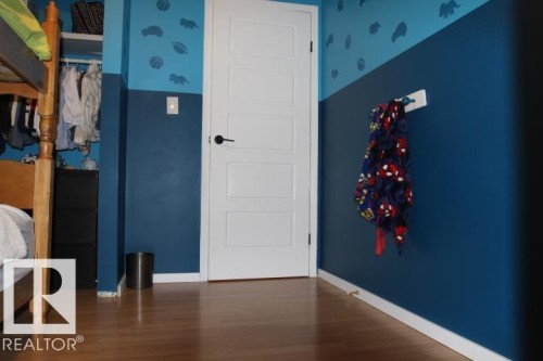 Wood-finish flooring with white trim, a white paneled door with black hardware, and an open closet with shelving - 64 Apache Crescent, Leduc, AB 