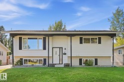 White exterior siding with black trim, a prominent front entrance with a glass insert, and a well-maintained green lawn - 
