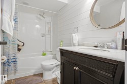 White bathtub and shower combination with a rain shower head, dark wood-finish vanity with a white countertop, and shiplap-style wall paneling - 