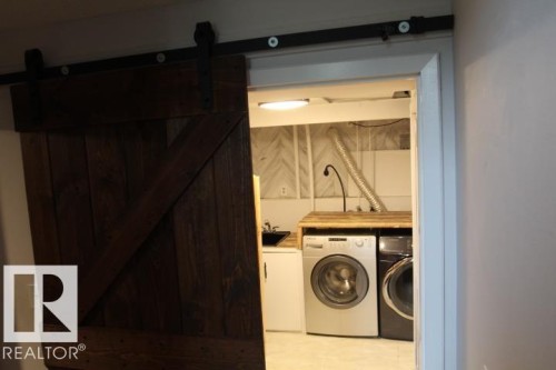 Barn-style sliding door with black hardware, wood-finish countertop, and full-size laundry appliances - 64 Apache Crescent, Leduc, AB 