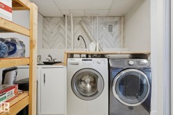 Dedicated laundry area featuring a utility sink with a stainless steel faucet, white base cabinetry with matte black hardware, and a wood-finish countertop - 