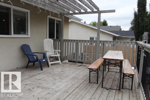 Expansive wood-finish deck with a wood pergola, solid railings, and an exterior wall featuring two white-framed windows - 64 Apache Crescent, Leduc, AB 