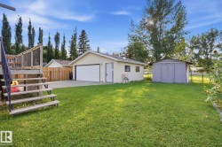 Detached garage with white overhead door, additional storage shed, and a wooden deck with railing - 