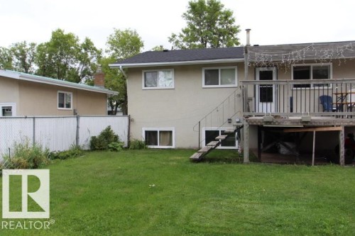 Expansive backyard featuring a manicured lawn, an elevated wooden deck, and a chain-link fence - 64 Apache Crescent, Leduc, AB 