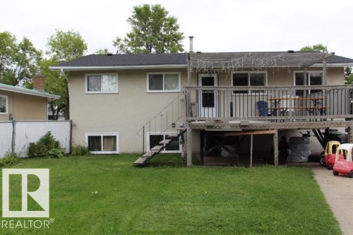 Rear exterior featuring a raised wooden deck with railings, a pergola, and a lower-level concrete patio - 64 Apache Crescent, Leduc, AB 
