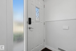 White paneled entry door with decorative glass inserts, sidelight with vertical reeded glass, and a modern black smart lock - 