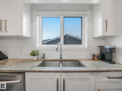 White cabinetry with gold-tone hardware, undermount stainless steel double-basin sink, and a white subway tile backsplash - 3807 Weidle Crescent Sw, Edmonton, AB 