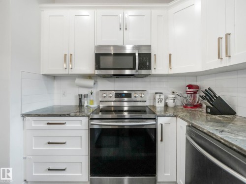 White shaker-style cabinetry with crown molding, stainless steel appliances, dark stone countertops, and white subway tile backsplash - 3807 Weidle Crescent Sw, Edmonton, AB 