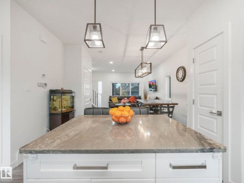 Kitchen island with a stone-finish countertop, white cabinetry, and linear pendant lighting fixtures - 3807 Weidle Crescent Sw, Edmonton, AB 