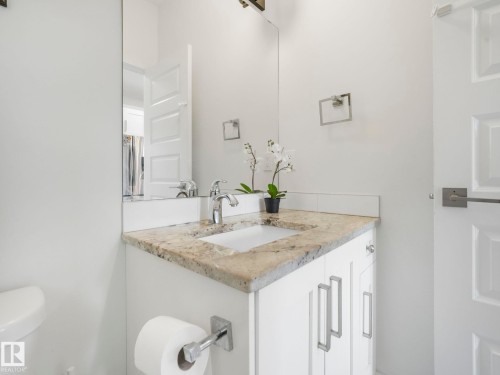 White vanity with a light-toned stone countertop, integrated sink, chrome faucet, and rectangular mirror - 3807 Weidle Crescent Sw, Edmonton, AB 