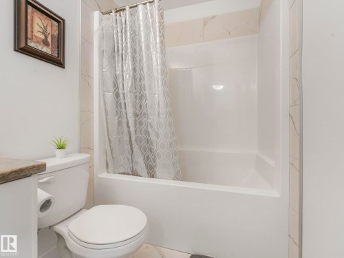 White toilet with a built-in toilet paper holder and a stone-look countertop - 3807 Weidle Crescent Sw, Edmonton, AB 