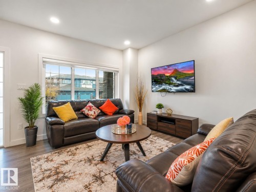 Wood-finish flooring, recessed lighting, large windows with white trim, and a wall-mounted media console - 3807 Weidle Crescent Sw, Edmonton, AB 